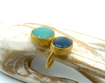 May include: A gold ring with two oval-shaped gemstones. The larger stone is a light blue-green color, and the smaller stone is a dark blue color.