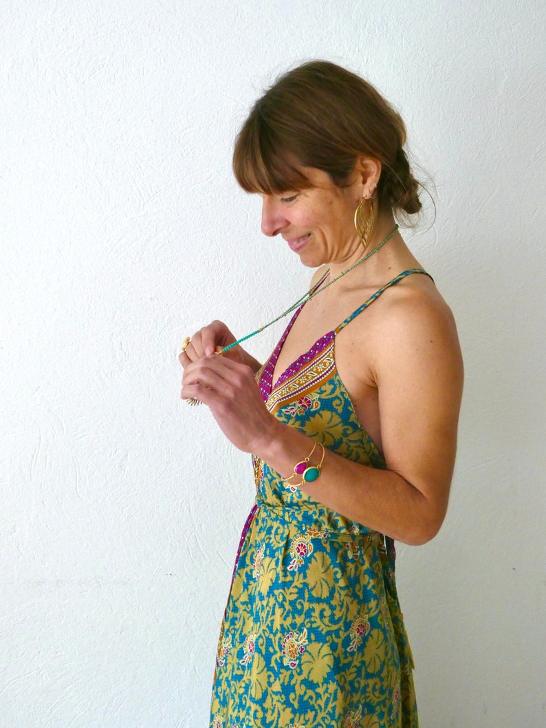 May include: A woman wearing a yellow and blue floral print dress with a pink and purple trim. She is wearing a turquoise and gold necklace and a gold bracelet with turquoise and pink stones.