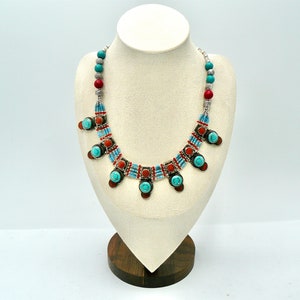 Op de afbeelding: Een turquoise en rode kralenketting met zilveren accenten. De ketting heeft een rij turquoise en rode kralen met zilveren accenten en een hanger met een turquoise steen.