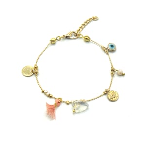 Puede incluir: Pulsera de cadena dorada con dijes, incluyendo un borla rosa, un cristal transparente, una moneda de oro, un dije de ojo azul y una perla blanca.