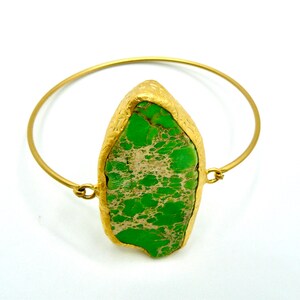 Puede incluir: Un brazalete de oro con una piedra grande verde y blanca en el centro.