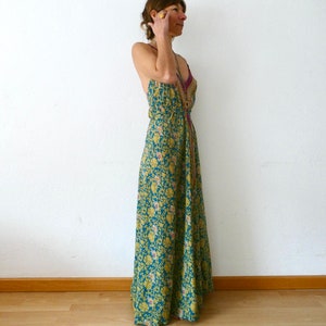 May include: A woman wearing a long, flowing maxi dress with a floral pattern in shades of blue, green, and yellow. The dress has a halter neckline and a fitted bodice.