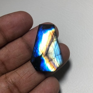 Könnte beinhalten: Ein blauer und goldener Labradorit-Cabochon mit einer facettierten, tropfenförmigen Form.