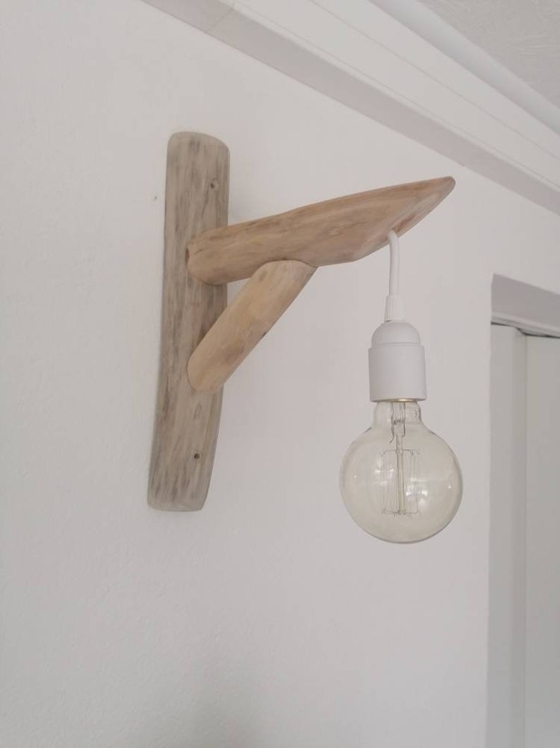 May include: A rustic wooden wall sconce with a single light bulb hanging from it. The sconce is made of driftwood and has a natural, weathered finish.