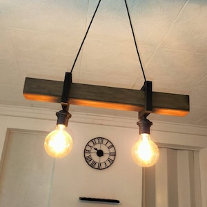 May include: A rustic wooden ceiling light fixture with two exposed light bulbs. The fixture is suspended from the ceiling by two black cords. The light bulbs are hanging from the fixture by black metal chains.