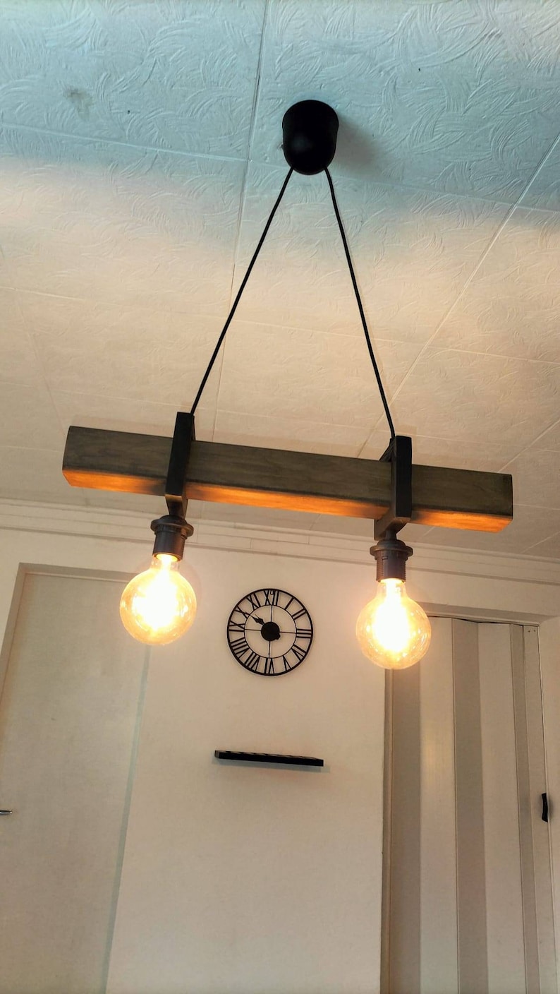 May include: A rustic wooden ceiling light fixture with two exposed light bulbs. The fixture is suspended from the ceiling by two black cords. The light bulbs are hanging from the fixture by black metal chains.