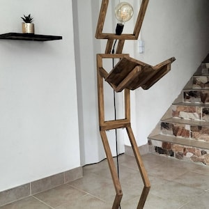 Peut inclure: Un lampadaire en bois en forme de personne tenant un livre. La lampe a une ampoule dans la t&ecirc;te et une base noire.