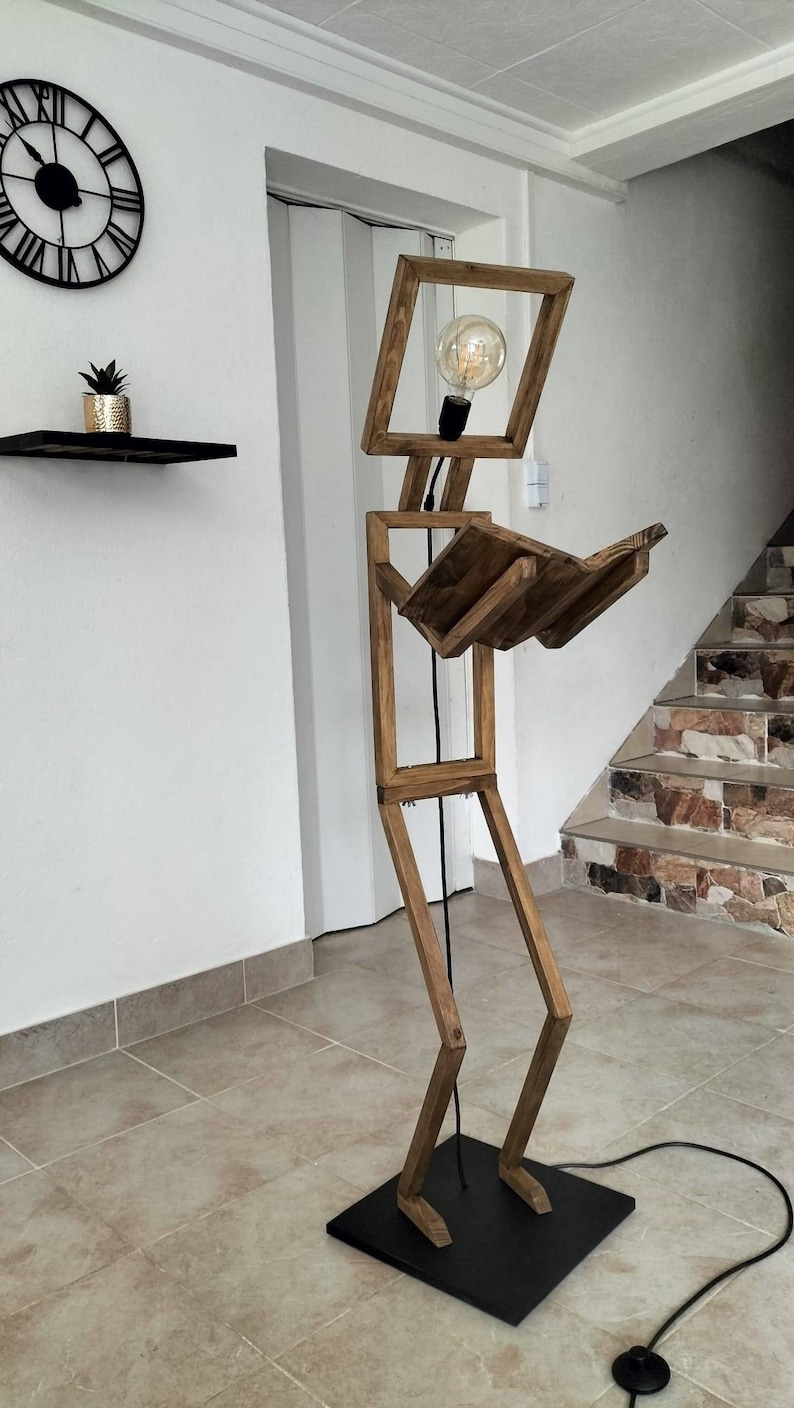 Peut inclure: Un lampadaire en bois en forme de personne tenant un livre. La lampe a une ampoule dans la t&ecirc;te et une base noire.