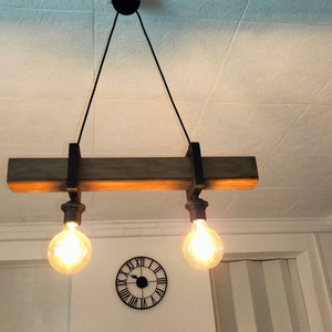 May include: A rustic wooden ceiling light fixture with two exposed light bulbs. The fixture is suspended from the ceiling by two black cords.