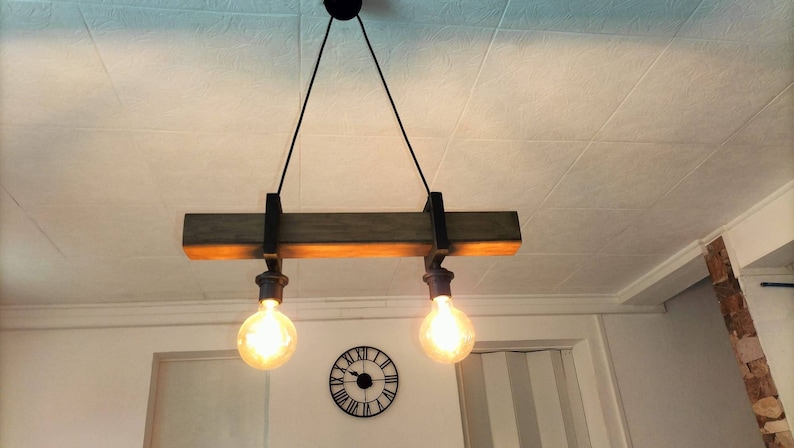 May include: A rustic wooden ceiling light fixture with two exposed light bulbs. The fixture is suspended from the ceiling by two black cords.