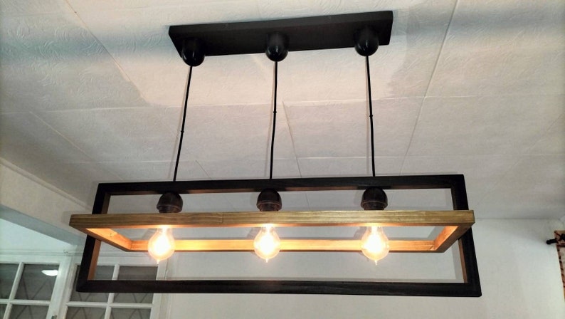 May include: A black rectangular frame chandelier with four light bulbs. The frame is made of wood with a natural finish and has a black metal outer frame.