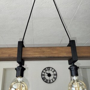 May include: A black pendant light fixture with two Edison bulbs hanging from a wooden beam. The fixture is suspended from the ceiling with black cords.