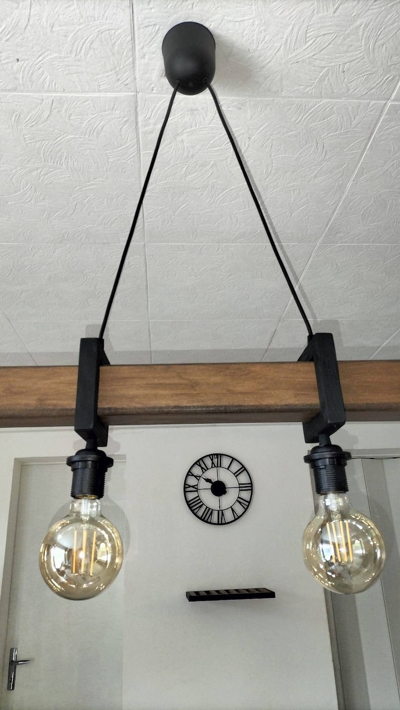 May include: A black pendant light fixture with two Edison bulbs hanging from a wooden beam. The fixture is suspended from the ceiling with black cords.