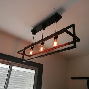 May include: A black metal and wood rectangular chandelier with four light bulbs. The chandelier has a geometric design with a square frame and a rectangular inner frame.