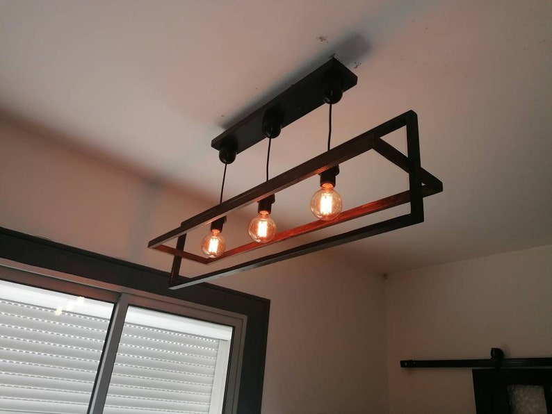 May include: A black metal and wood rectangular chandelier with four light bulbs. The chandelier has a geometric design with a square frame and a rectangular inner frame.