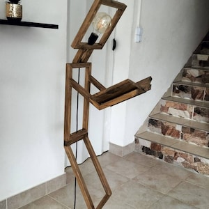 Peut inclure: Un lampadaire en bois en forme de personne tenant un livre. La lampe a une ampoule dans la t&ecirc;te et un cordon noir.