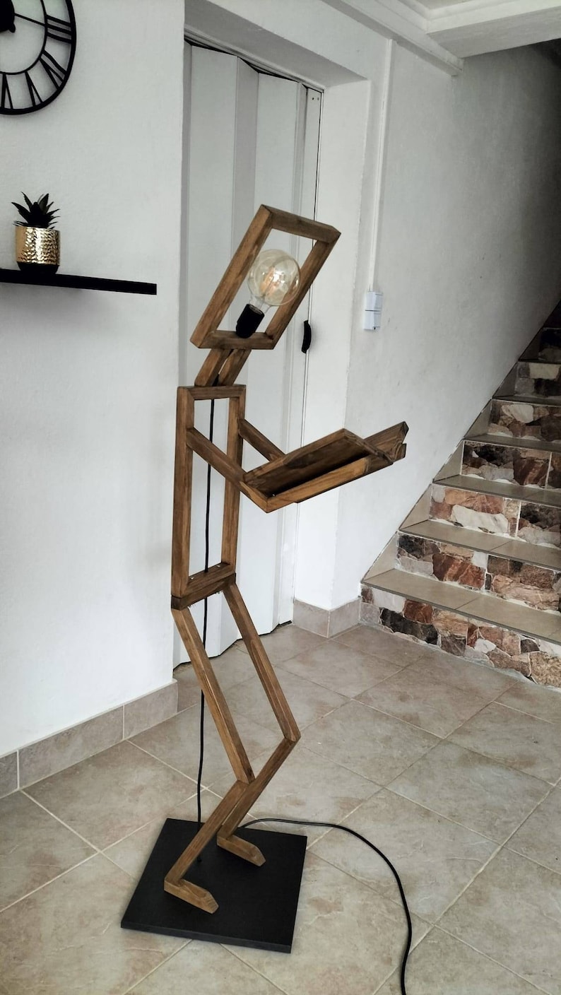Peut inclure: Un lampadaire en bois en forme de personne tenant un livre. La lampe a une ampoule dans la t&ecirc;te et un cordon noir.