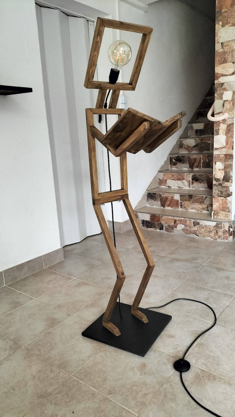 Peut inclure: Un lampadaire en bois en forme de personne lisant un livre. La lampe a une ampoule dans la t&ecirc;te et un cordon noir.