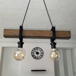 May include: A rustic wooden beam pendant light fixture with two Edison bulbs hanging from black cords. The fixture is suspended from the ceiling with black metal brackets.