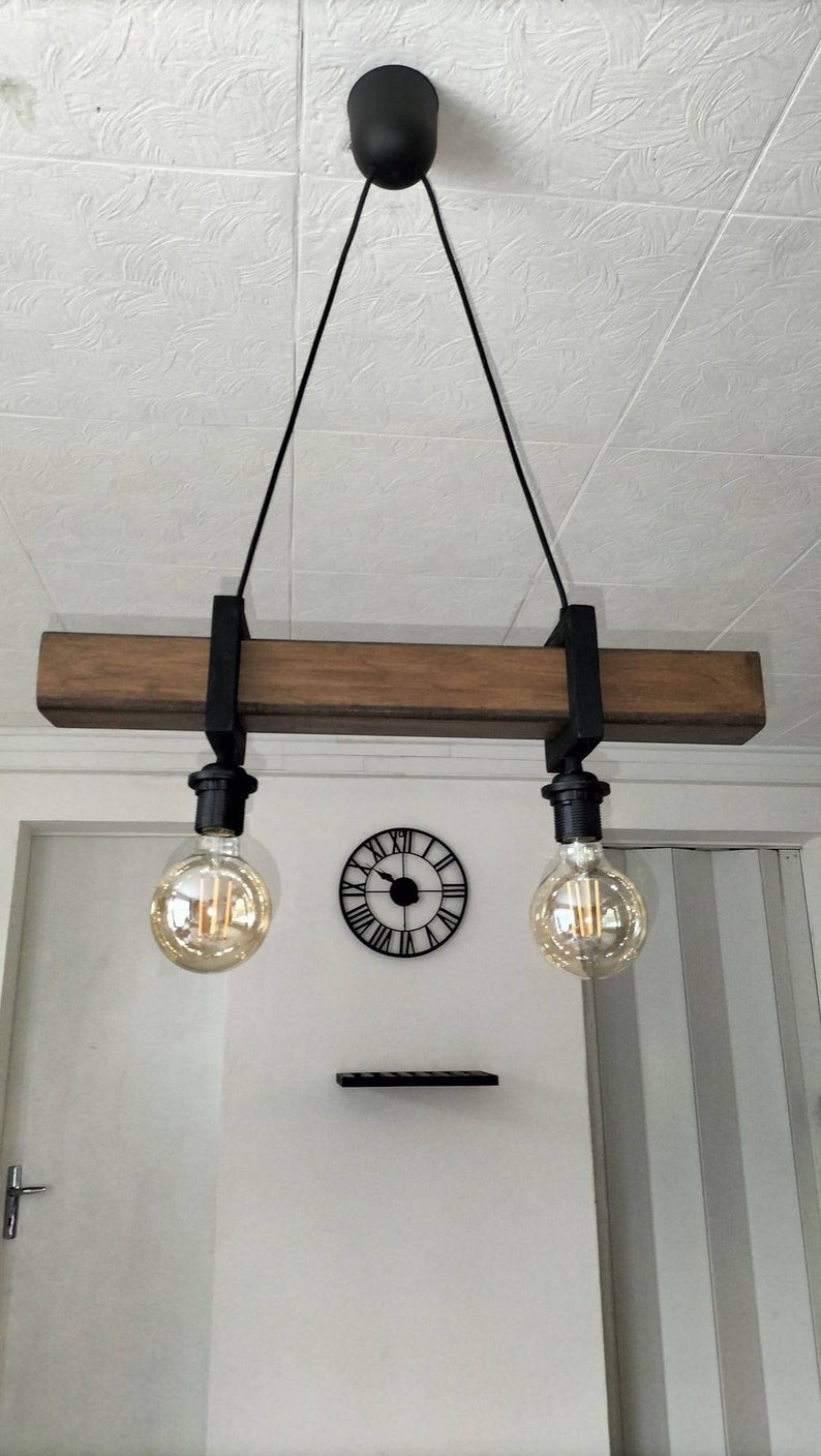 May include: A rustic wooden beam pendant light fixture with two Edison bulbs hanging from black cords. The fixture is suspended from the ceiling with black metal brackets.