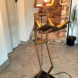 Peut inclure: Un lampadaire en bois en forme de personne lisant un livre. La lampe a une ampoule dans la t&ecirc;te et un cordon noir avec un interrupteur au pied.