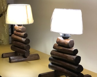 Puede incluir: Dos lámparas de mesa de madera con pantallas blancas. Las lámparas están hechas de troncos de madera apilados y tienen un aspecto rústico.