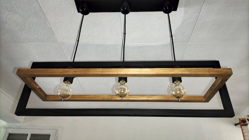 May include: A rectangular black and gold framed chandelier with three light bulbs.