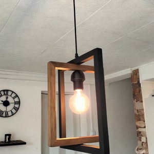 May include: A modern pendant light fixture with a black metal frame and a wood accent. The light fixture has a single bulb and hangs from a black cord.