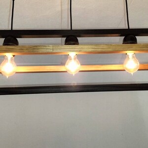 May include: A rectangular wood and metal chandelier with three light bulbs. The chandelier has a dark wood frame and a light wood top.