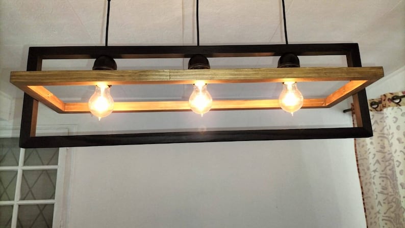 May include: A rectangular wood and metal chandelier with three light bulbs. The chandelier has a dark wood frame and a light wood top.