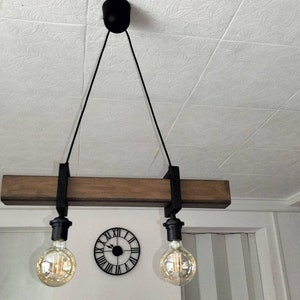May include: A rustic wooden ceiling light fixture with two black metal hanging cords and Edison bulb light fixtures. The fixture is suspended from the ceiling with black cords.