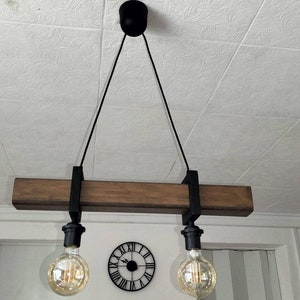 May include: A rustic wooden pendant light fixture with two black metal light sockets and exposed bulbs. The fixture is suspended from the ceiling by two black cords.