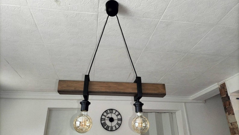 May include: A rustic wooden pendant light fixture with two black metal light sockets and exposed bulbs. The fixture is suspended from the ceiling by two black cords.