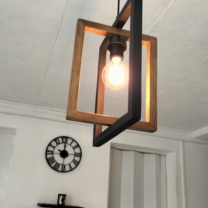 May include: A black and wood pendant light fixture with a single light bulb. The light fixture is hanging from the ceiling and is in a room with white walls.