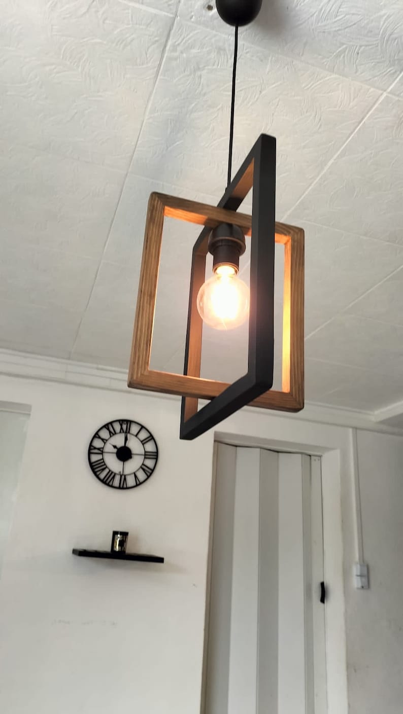 May include: A black and wood pendant light fixture with a single light bulb. The light fixture is hanging from the ceiling and is in a room with white walls.