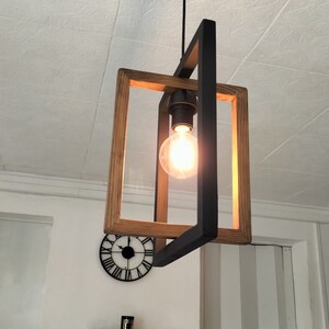 May include: A wooden and black metal pendant light fixture with a single light bulb. The light fixture is hanging from a ceiling with a white textured surface.