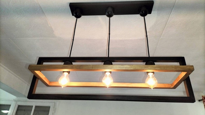 May include: A rectangular wood and black metal chandelier with three light bulbs. The chandelier has a rustic, industrial style.