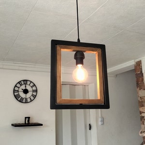 May include: A black framed pendant light with a wood accent and a clear light bulb. The light is hanging from a black cord and is suspended from a black ceiling fixture.