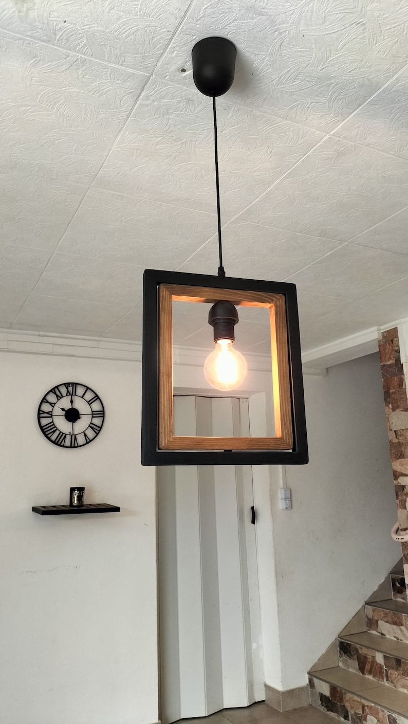 May include: A black framed pendant light with a wood accent and a clear light bulb. The light is hanging from a black cord and is suspended from a black ceiling fixture.