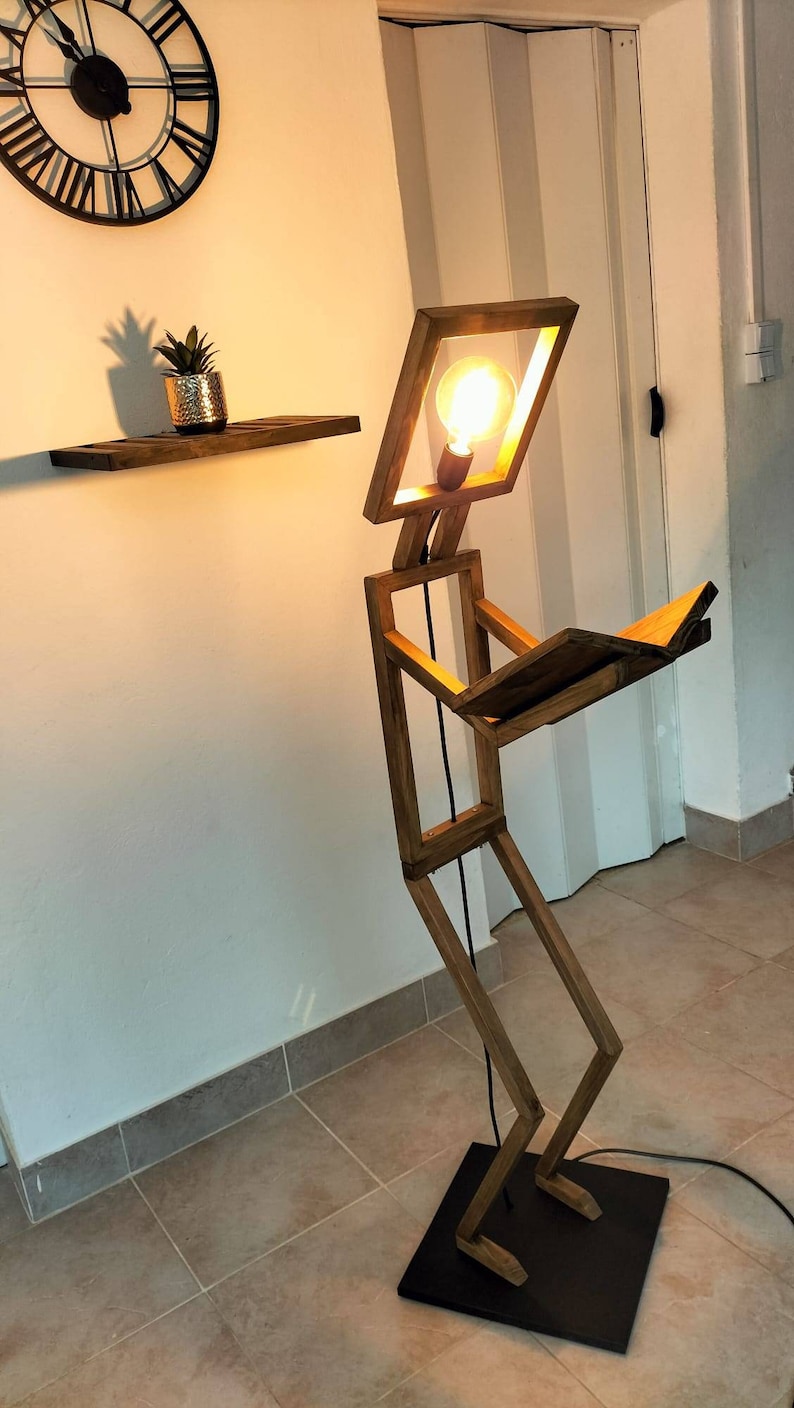 Peut inclure: Une lampe en bois en forme de personne lisant un livre. La lampe a une ampoule dans la t&ecirc;te et une base noire.