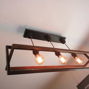 May include: A rectangular black metal frame with a wooden top holds four light bulbs. The light bulbs are hanging from black cords and are turned on, illuminating the room.
