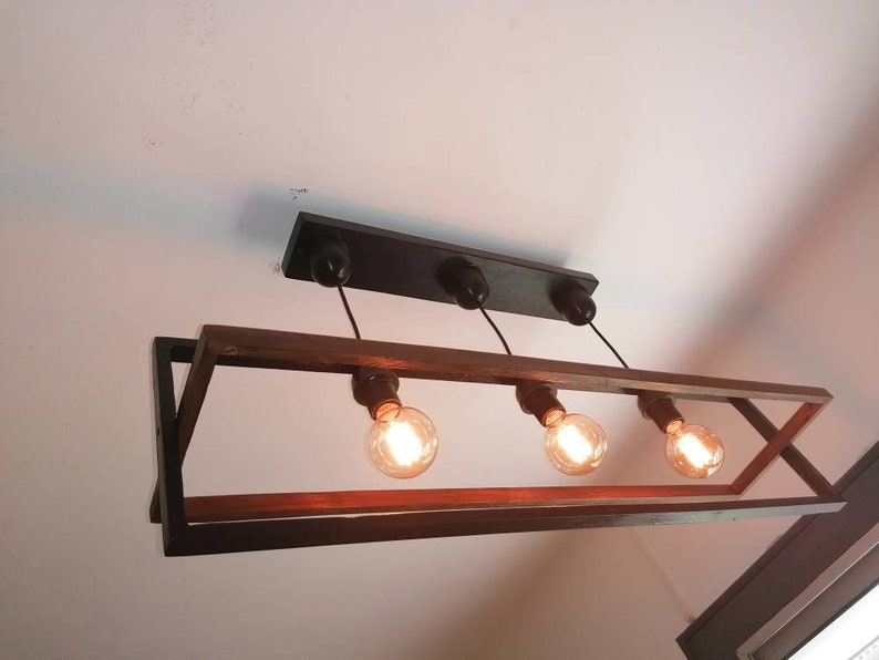 May include: A rectangular black metal frame with a wooden top holds four light bulbs. The light bulbs are hanging from black cords and are turned on, illuminating the room.