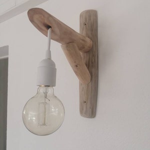 May include: A rustic wooden wall sconce with a white cord and a clear glass light bulb. The sconce is made from natural driftwood and has a unique, organic shape.