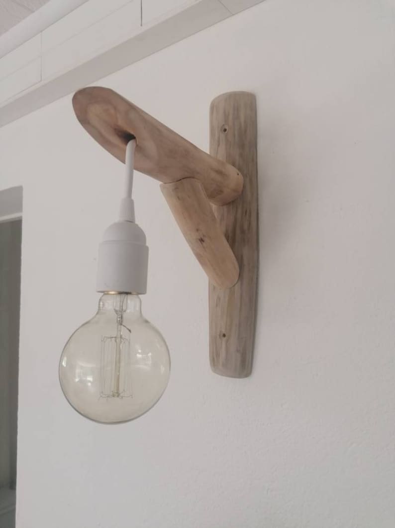 May include: A rustic wooden wall sconce with a white cord and a clear glass light bulb. The sconce is made from natural driftwood and has a unique, organic shape.