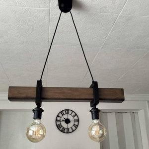 May include: A rustic wooden ceiling light fixture with two black metal lampshades and Edison bulbs. The fixture is suspended from the ceiling by two black cords.