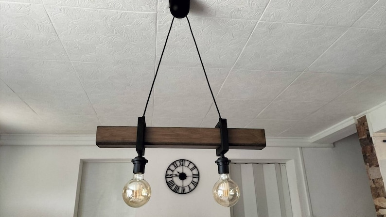 May include: A rustic wooden ceiling light fixture with two black metal lampshades and Edison bulbs. The fixture is suspended from the ceiling by two black cords.