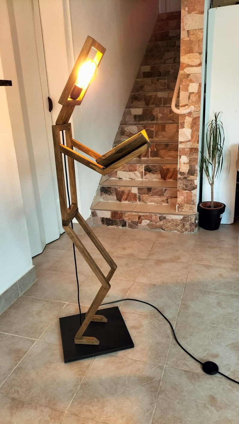 Peut inclure: Un lampadaire en bois en forme de personne lisant un livre. La lampe a une ampoule chaude et un cordon noir.