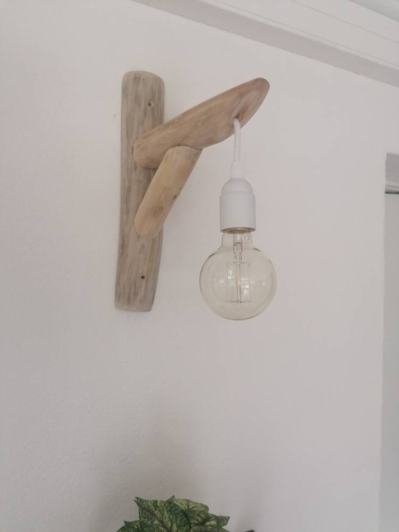 May include: A wall-mounted light fixture made from driftwood with a single light bulb hanging from it.