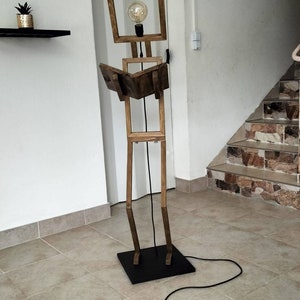 Peut inclure: Un lampadaire en bois en forme de personne tenant un livre. La lampe a une ampoule dans la t&ecirc;te et un cordon noir.
