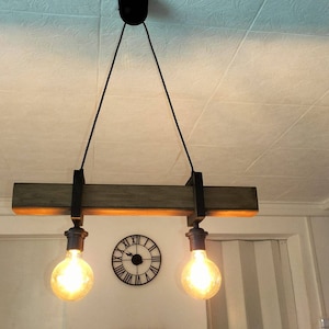 May include: A rustic wooden ceiling light fixture with two exposed bulbs hanging from black cords. The fixture is suspended from the ceiling with black metal brackets.